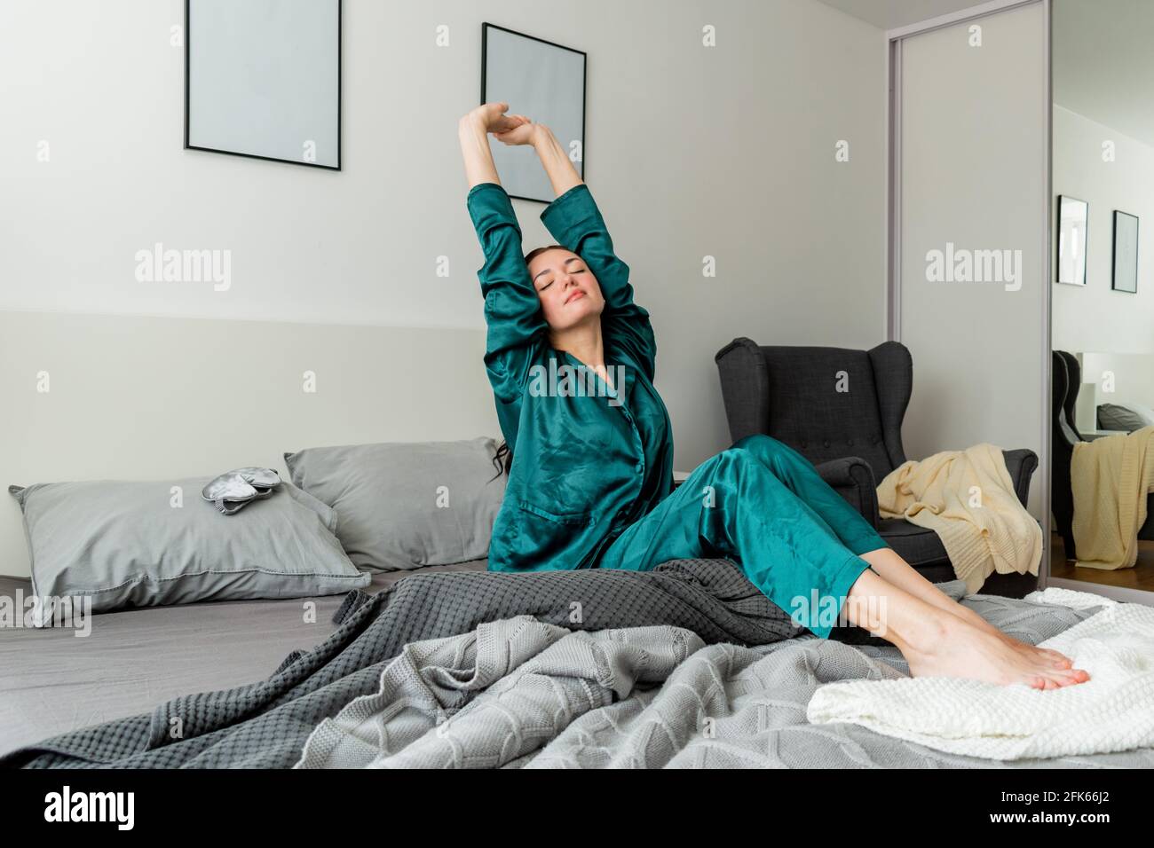 Jeune femme dans des yawns de pyjama en soie tout en étant assise dans un confortable lit doux. Banque D'Images