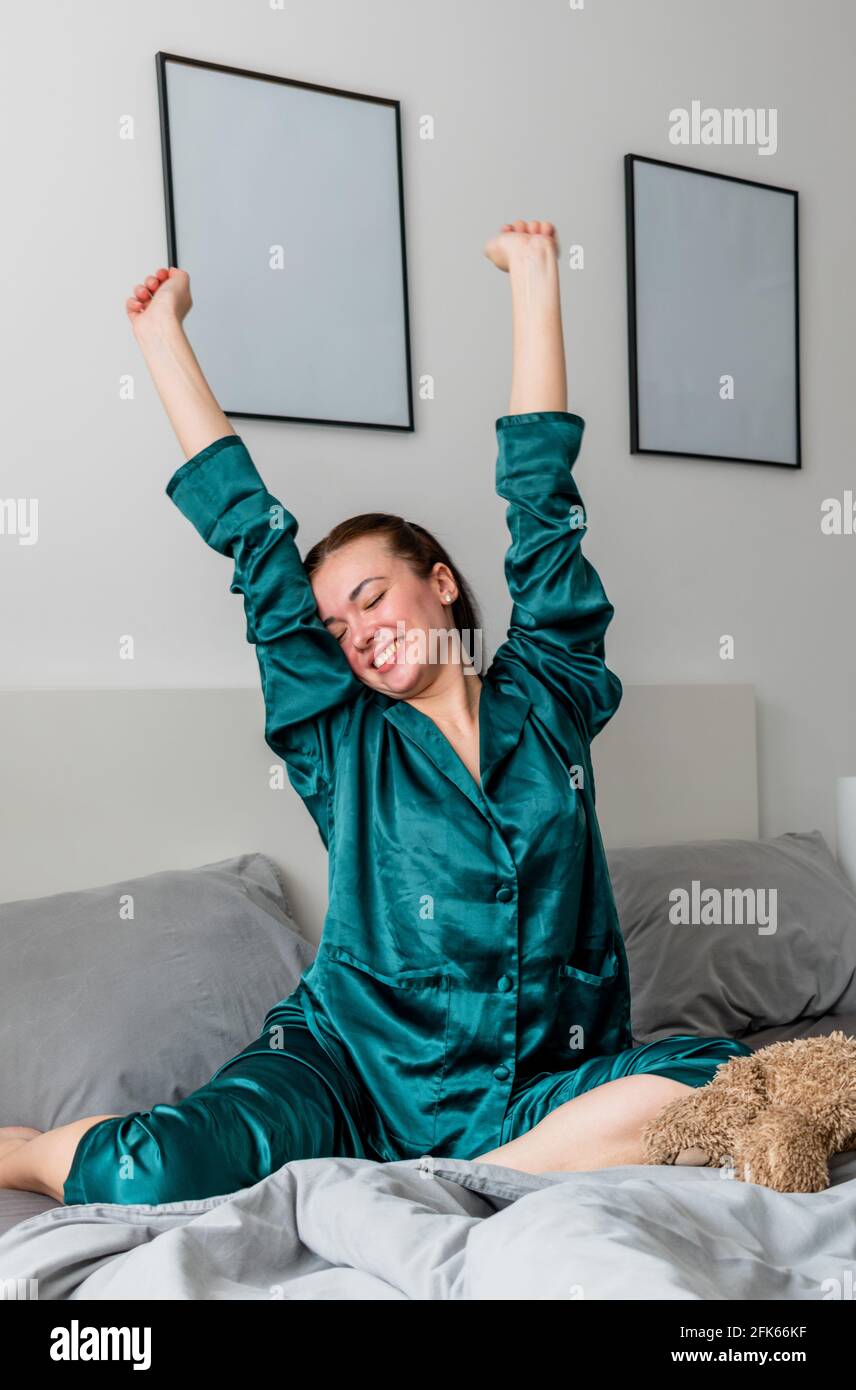 Jeune femme dans des yawns de pyjama en soie tout en étant assise dans un confortable lit doux. Banque D'Images