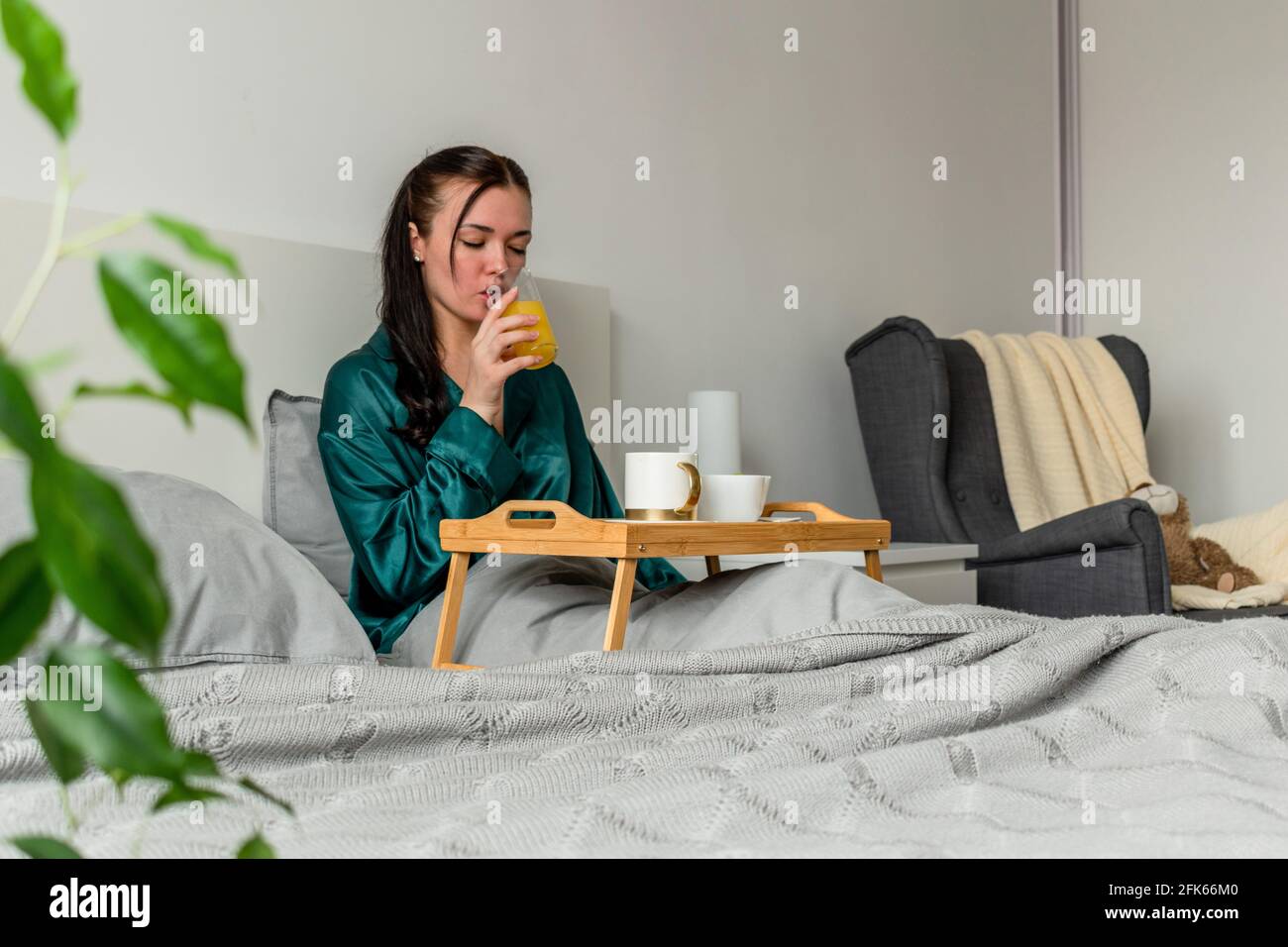 Jeune femme en pyjama de soie mangeant son petit déjeuner tout en étant au lit. Concept bien-être. Banque D'Images