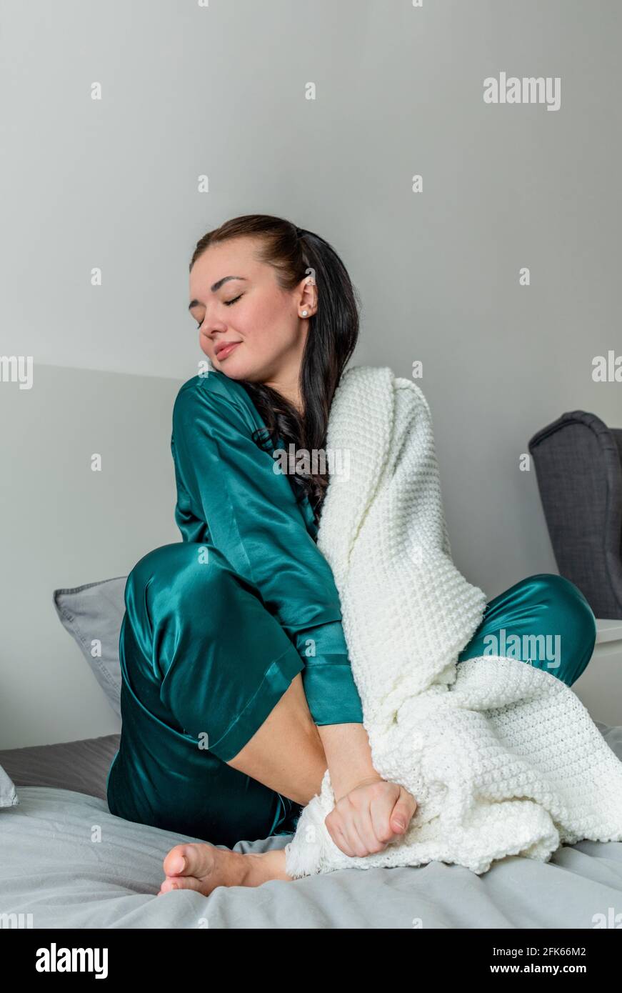 La jeune femme est enveloppée de tissu écossais blanc tout en étant assise sur le lit dans la chambre. Banque D'Images