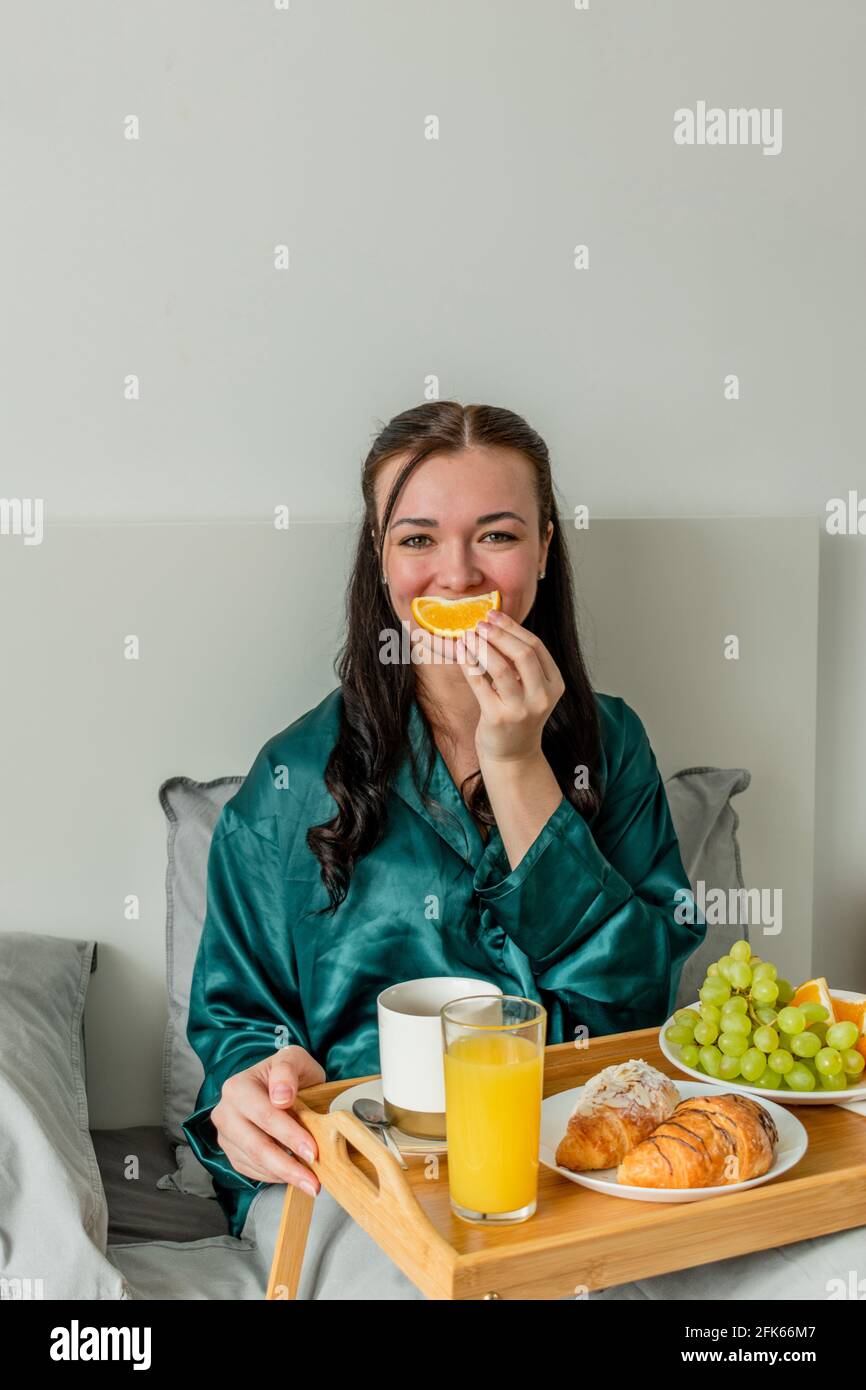 La jeune femme rit et tient une orange devant sa bouche. Concept de bien-être et zone de confort à la maison. Banque D'Images