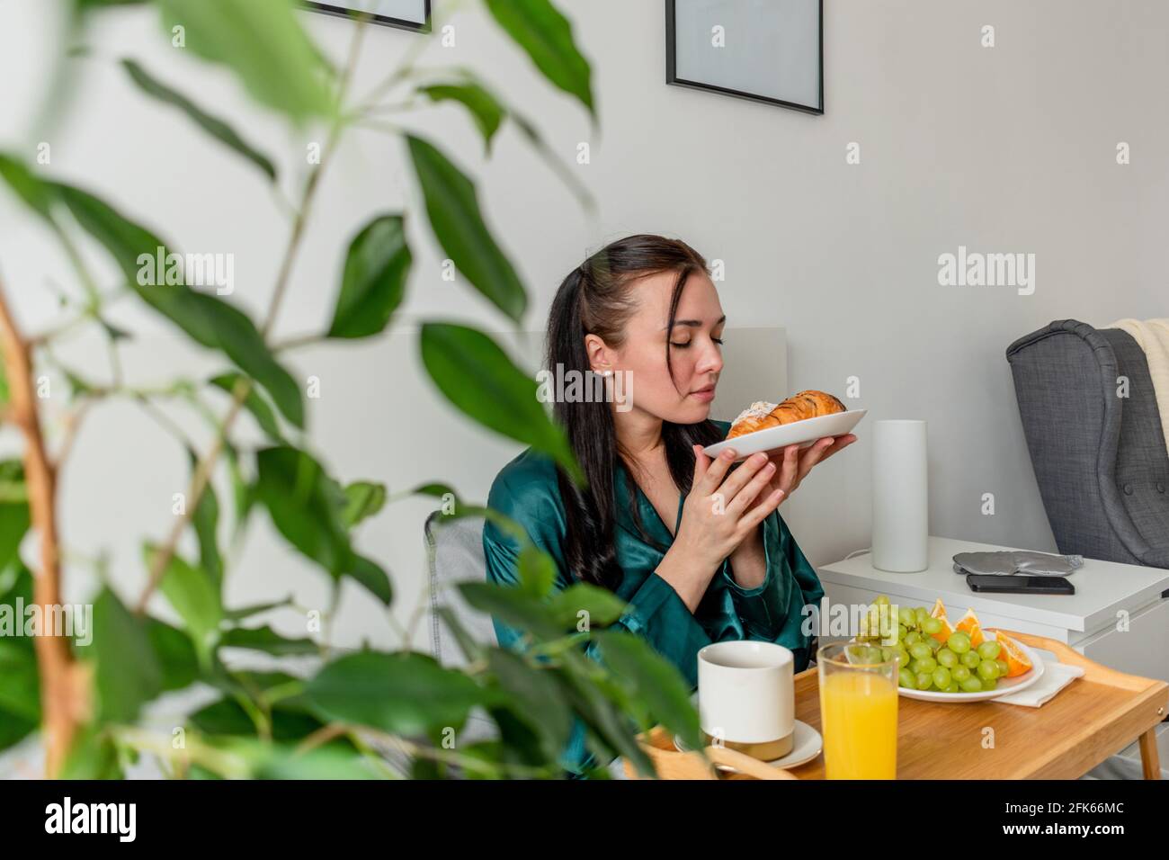 Jeune femme en pyjama de soie a un petit déjeuner sain tout en étant allongé sur le lit dans la chambre. Concept de bien-être à la maison. Santé émotionnelle d'une jeune femme Banque D'Images