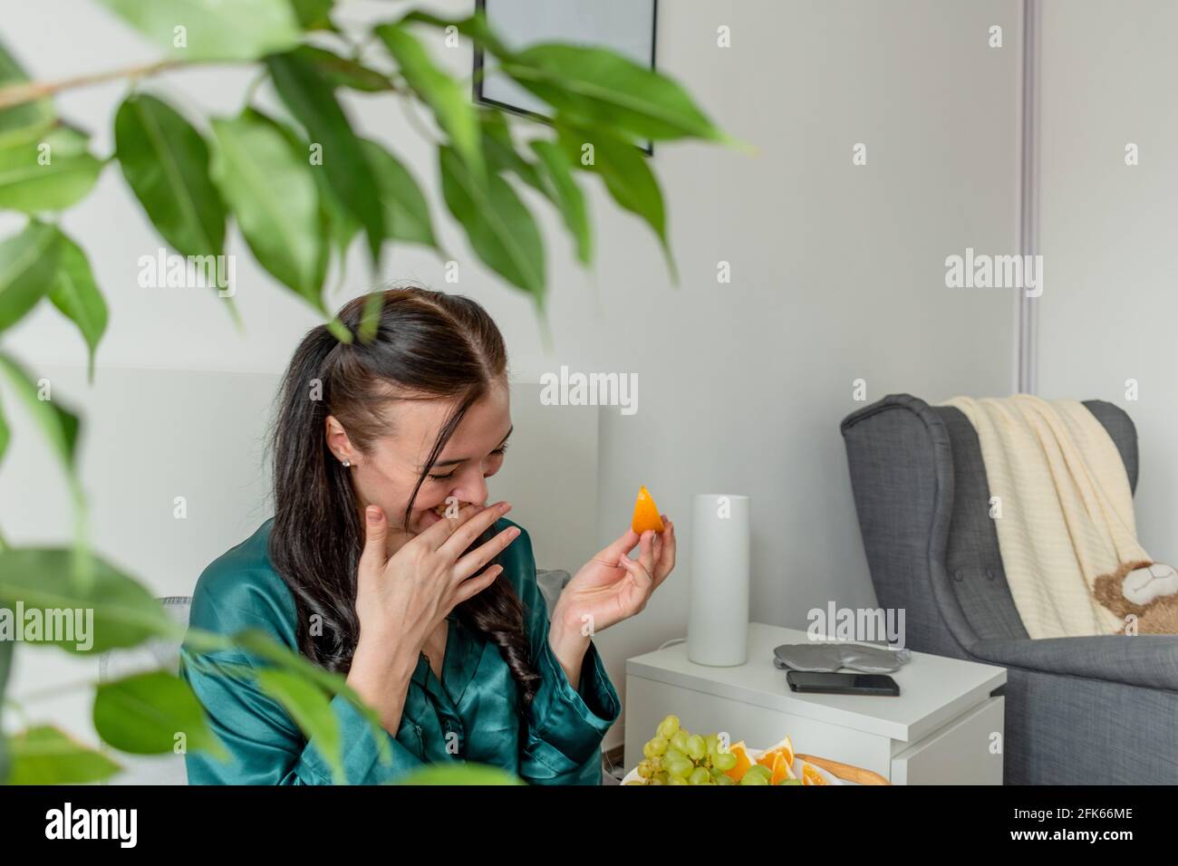 Jeune femme en pyjama de soie a un petit déjeuner sain tout en étant allongé sur le lit dans la chambre. Concept de bien-être à la maison. Santé émotionnelle d'une jeune femme Banque D'Images