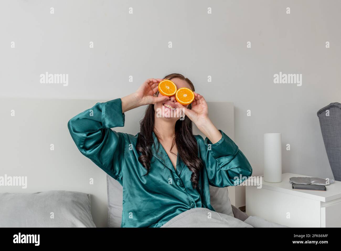 La jeune femme rit et tient les oranges près de ses yeux. Concept de bien-être et zone de confort à la maison. Banque D'Images