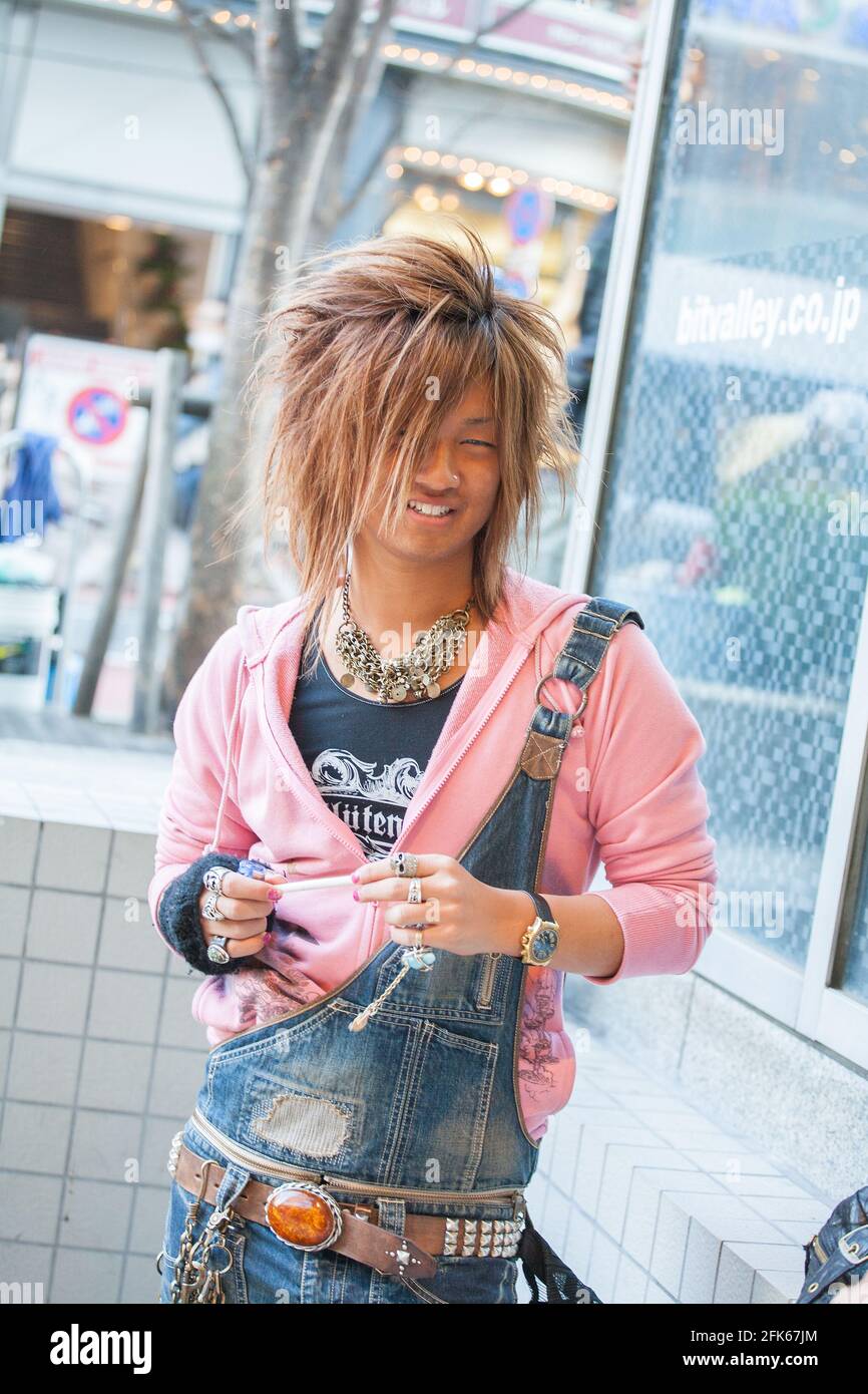 Gyaruo japonais bronzé avec de grands cheveux, le sweat à capuche rose, les salopettes, les anneaux et les colliers poses pour caméra à Shibuya, Tokyo, Japon Banque D'Images