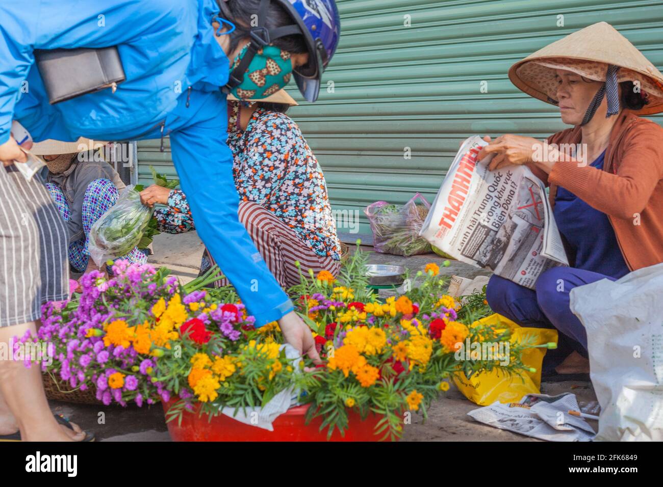 Femme vietnamienne portant un casque de moto et un masque facial choisissant des fleurs du fleuriste sur le côté de la route, Hoi an, Vietnam Banque D'Images