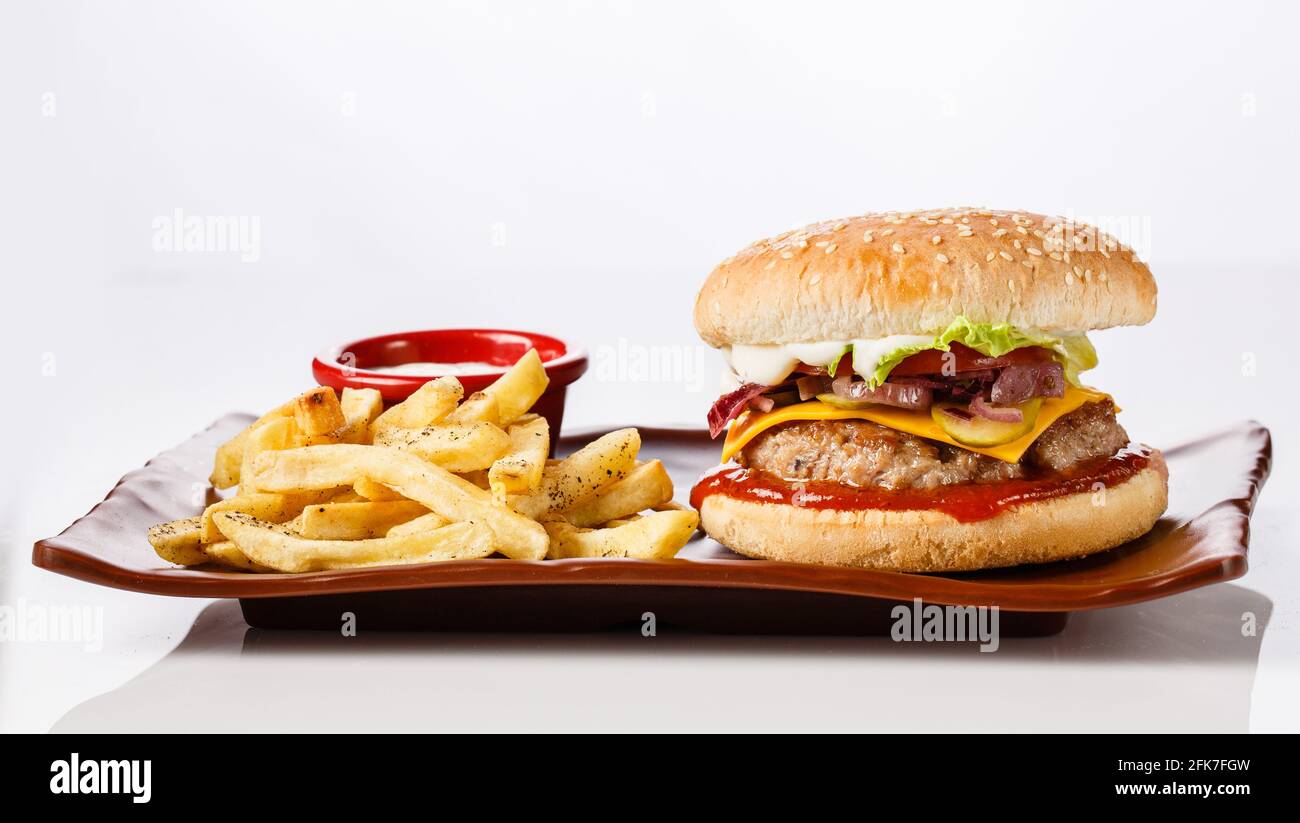 Hamburger. Côtelette de porc juteuse, cheddar, oignons croquants, laitue enveloppée dans un pain sous deux sauces. Servi avec des frites et de la sauce à la crème. Banque D'Images