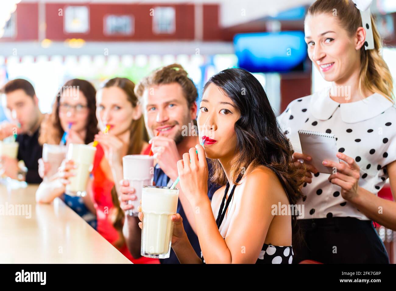 Des amis ou des couples eating fast food et de boire des milk-shakes sur bar en restauration rapide américaine diner, la serveuse est prise des commandes Banque D'Images