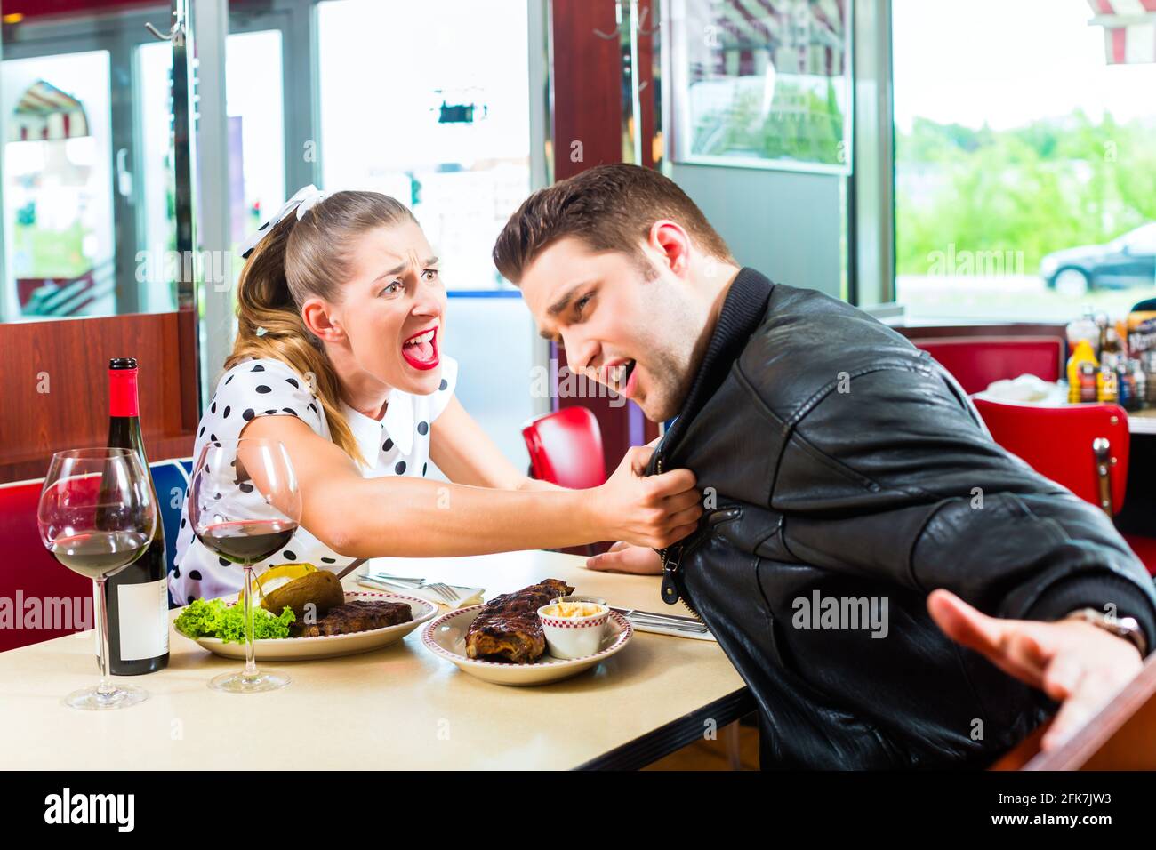 Jeune couple eating fast food et de boire du vin rouge dans un fast food American retro diner soutient Banque D'Images