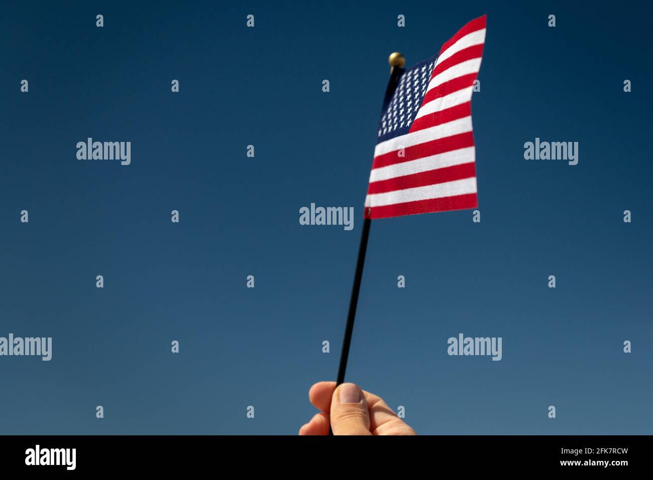 Close-up of woman's hand holding up un petit drapeau américain contre le ciel bleu. Banque D'Images