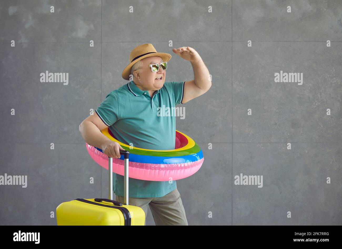 Drôle homme âgé dans un cercle gonflable et avec une valise regarde en arrière-plan. Banque D'Images