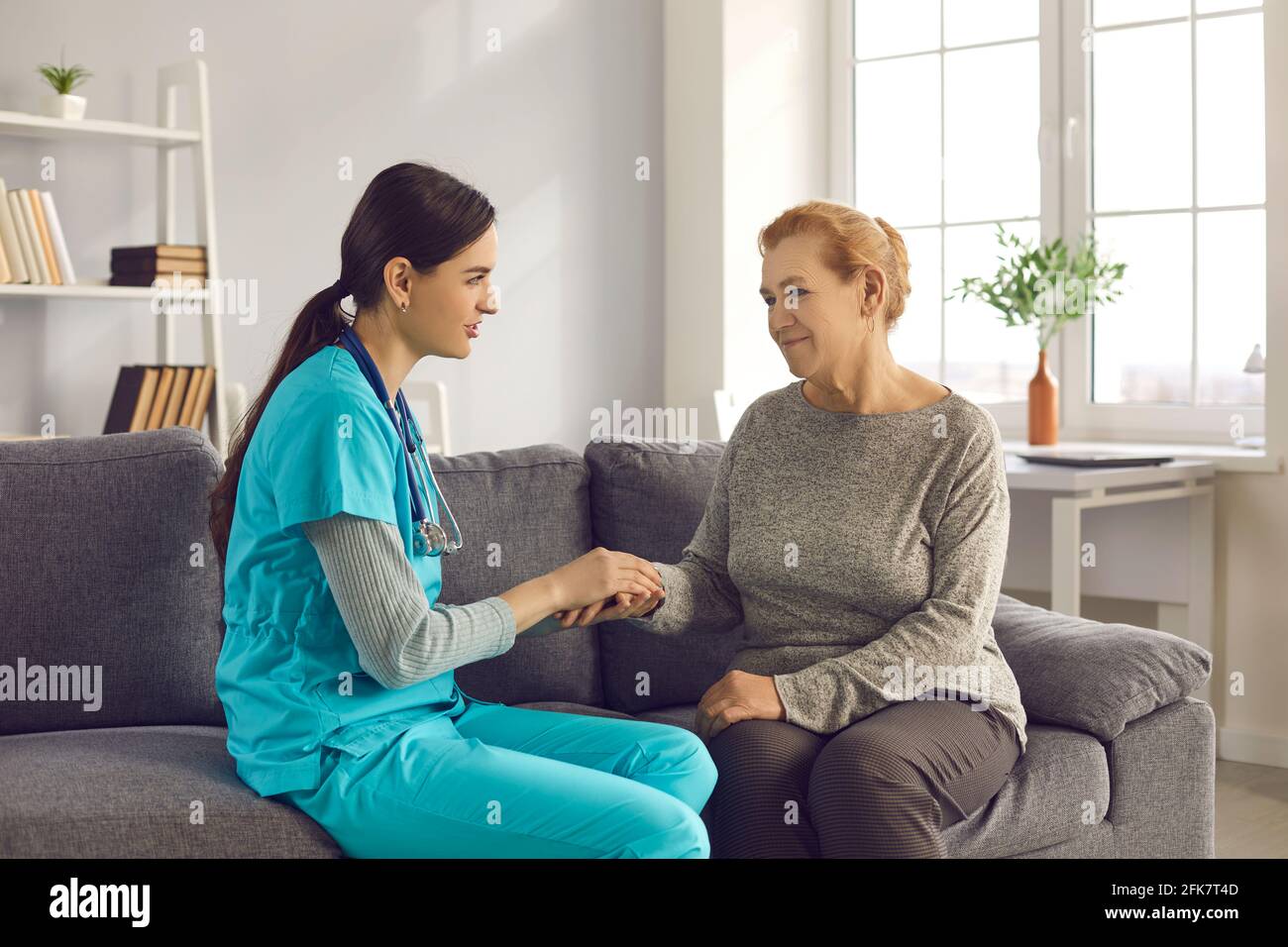 Une infirmière soutient une patiente âgée qui tient la main lors d'une visite médicale à domicile. Banque D'Images