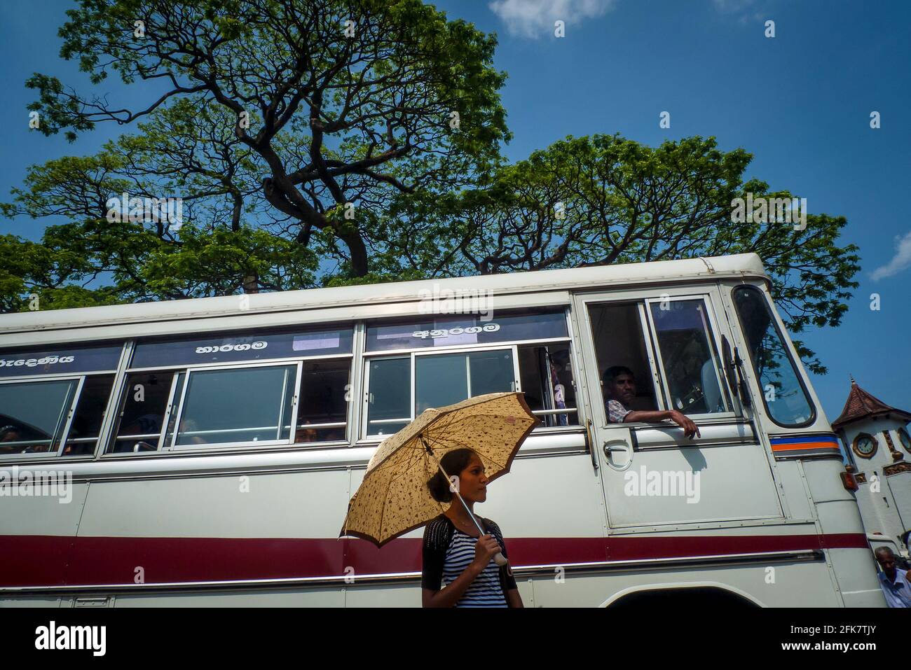 Kandy, Sri lanka: Une femme s'abite du soleil avec un parapluie en attendant de prendre le bus Banque D'Images