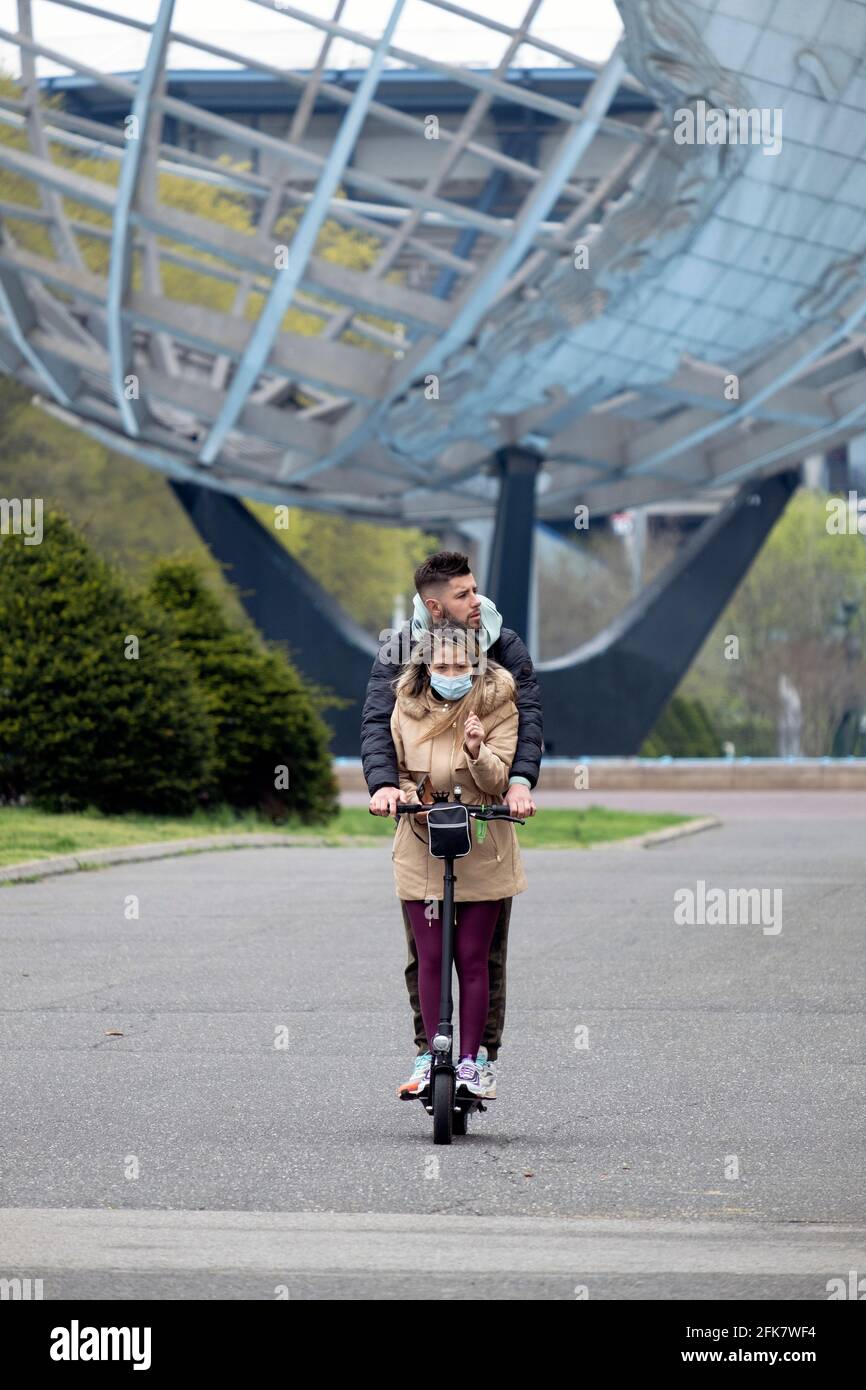 Avec Unisphere en arrière-plan, un couple se déplace ensemble sur un scooter motorisé. À Flushing Meadows Corona Park, Queens, New York. Banque D'Images