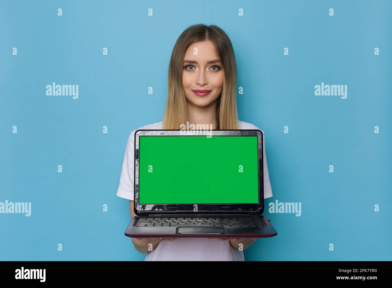 Belle jeune femme tient un ordinateur portable avec un cri vert. Taille haute studio tourné sur fond bleu. Banque D'Images