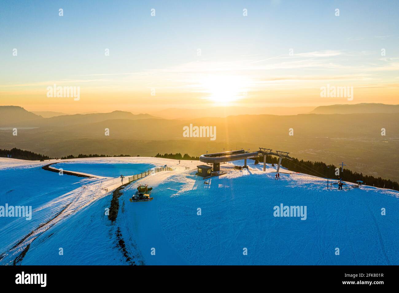 Prise de vue aérienne d'une station de remontée mécanique au sommet d'une montagne enneigée au lever/coucher du soleil. Banque D'Images