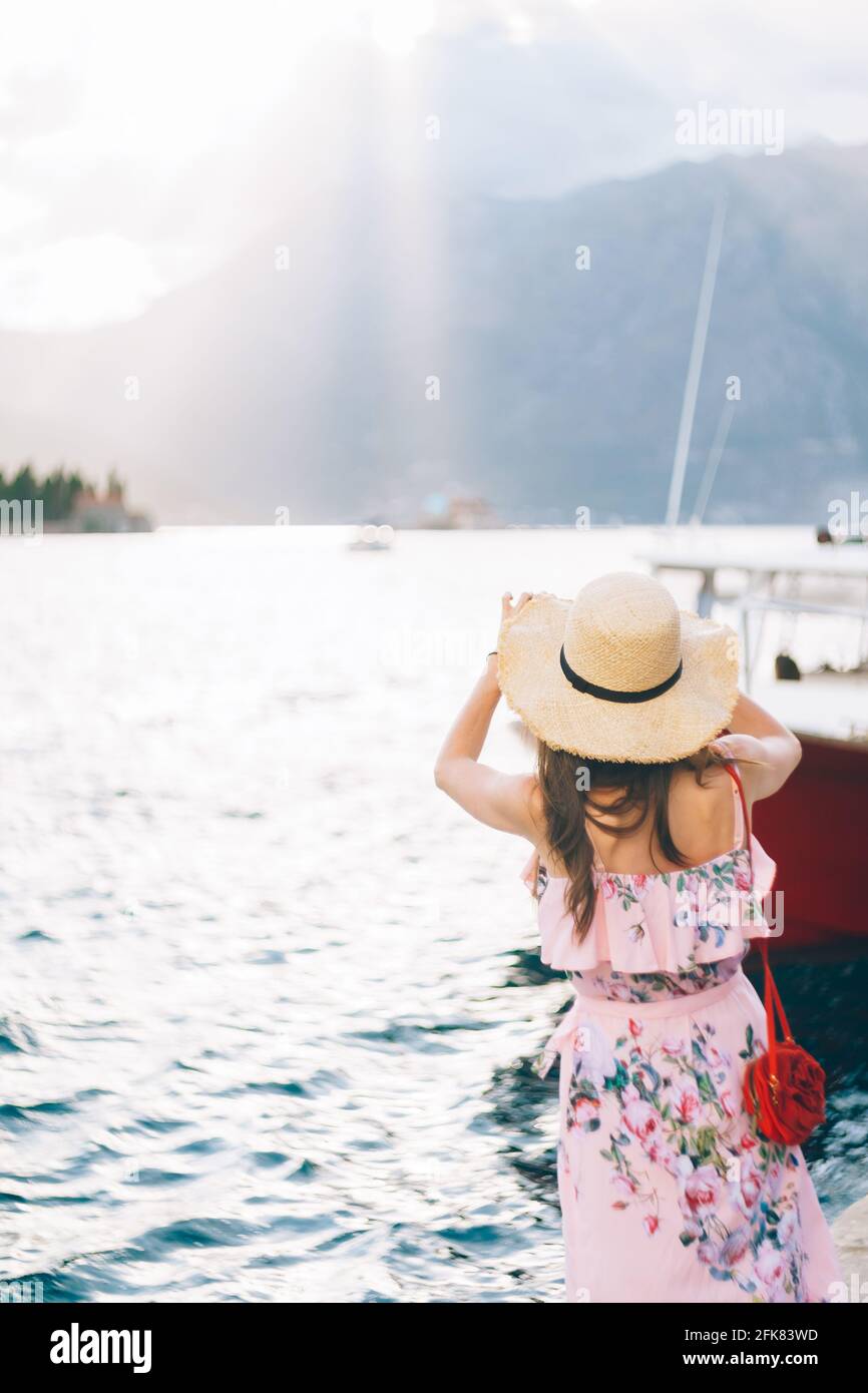 Une femme en robe et un chapeau de paille se tient sur le rivage de la baie  et prend des photos de l'île, vue arrière Photo Stock - Alamy