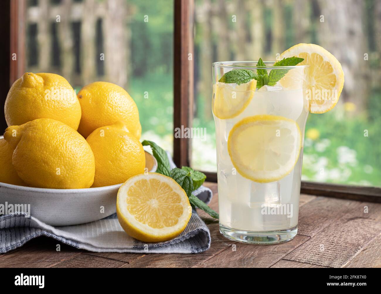 Verre de limonade et de citrons faits maison sur une table en bois par une fenêtre avec une scène rurale d'arrière-plan Banque D'Images