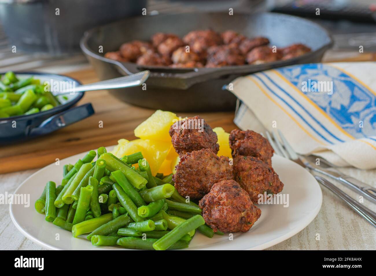 repas maison frais cuisiné avec boulettes de viande frites, haricots verts et pommes de terre bouillies servis sur une assiette avec une casserole sur le fond de la table de cuisine Banque D'Images
