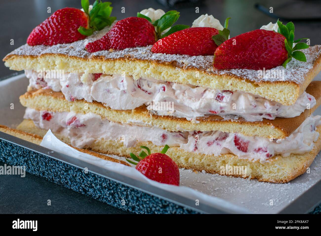 gâteau à la crème de fraise maison fait avec de la pâte de biscuit frais et servi avec des fraises fraîches sur une table de cuisine rustique arrière-plan Banque D'Images