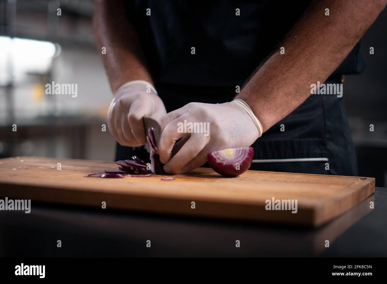 gros plan du chef cuisinier mains dans des gants de découpe ou hachez l'oignon rouge dans la cuisine Banque D'Images