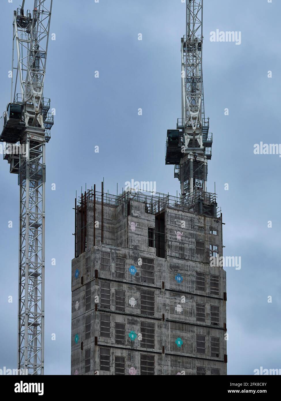 Une paire de grues à tour, travaillant pour construire un noyau central de bâtiment portant des logos Android, contre un ciel gris couvert. Banque D'Images