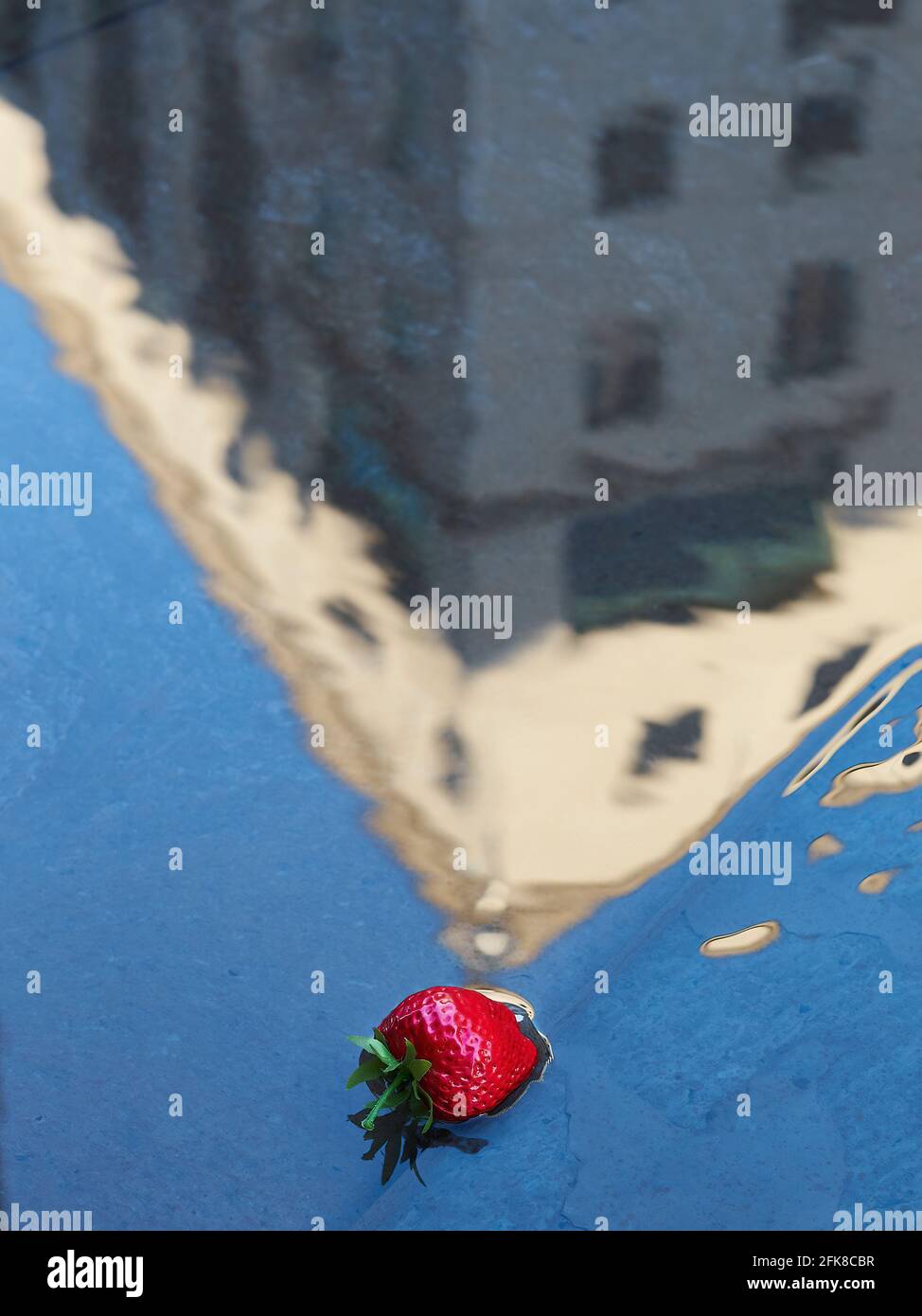 Une de ces choses étranges que l'on voit dans une grande ville - une fraise (peut-être fausse?) flottant dans un étang qui reflète un bâtiment voisin. Banque D'Images