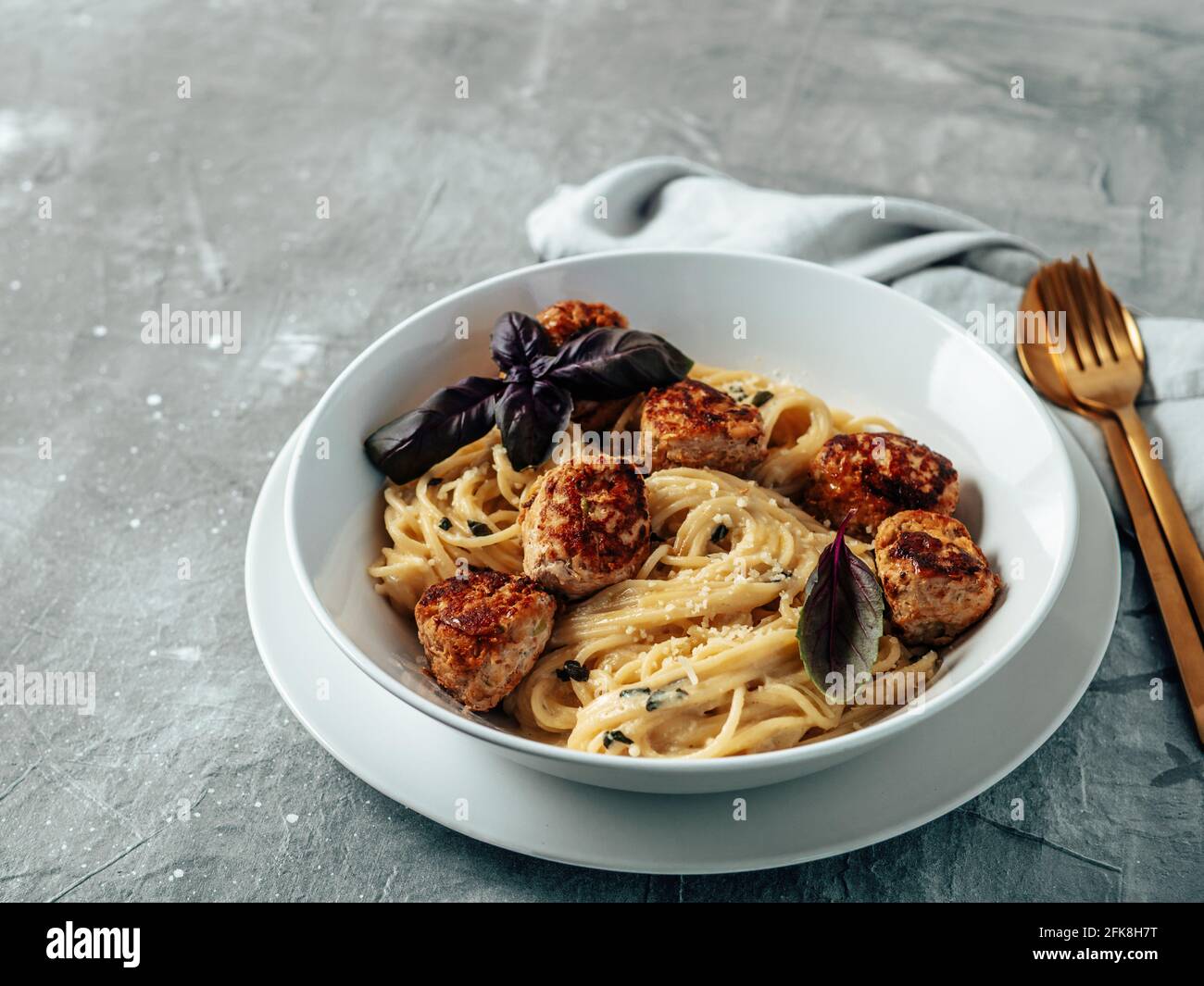 Boulettes de parmesan de courgettes aux pâtes Carbonara dans une assiette blanche sur fond gris. Vue rapprochée de la carbonara crémeuse avec espace de copie restant Banque D'Images