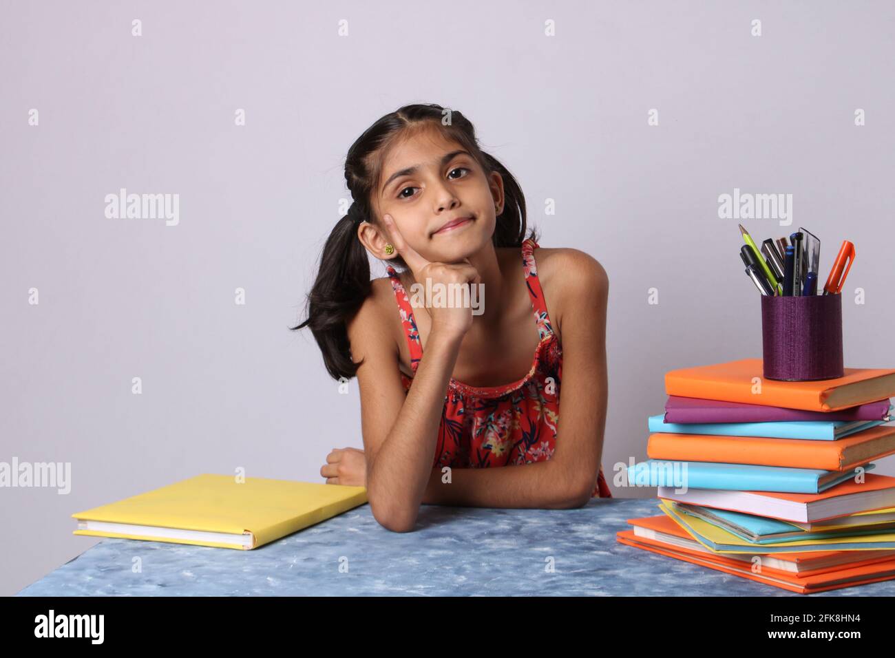 petite fille indienne pensant ou rêvant pendant la préparation des devoirs. avec pile de livres Banque D'Images