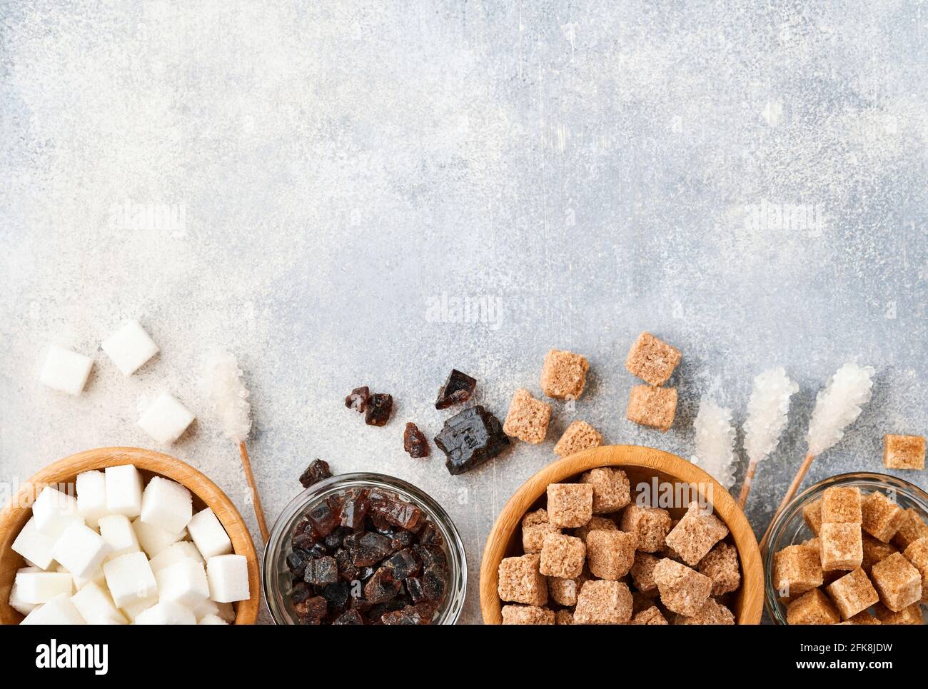 Sucre blanc, cubes de sucre de canne, caramel dans un bol en bambou sur fond de béton de table gris. Différents types de sucre assortis. Vue de dessus ou plan de travail. Banque D'Images