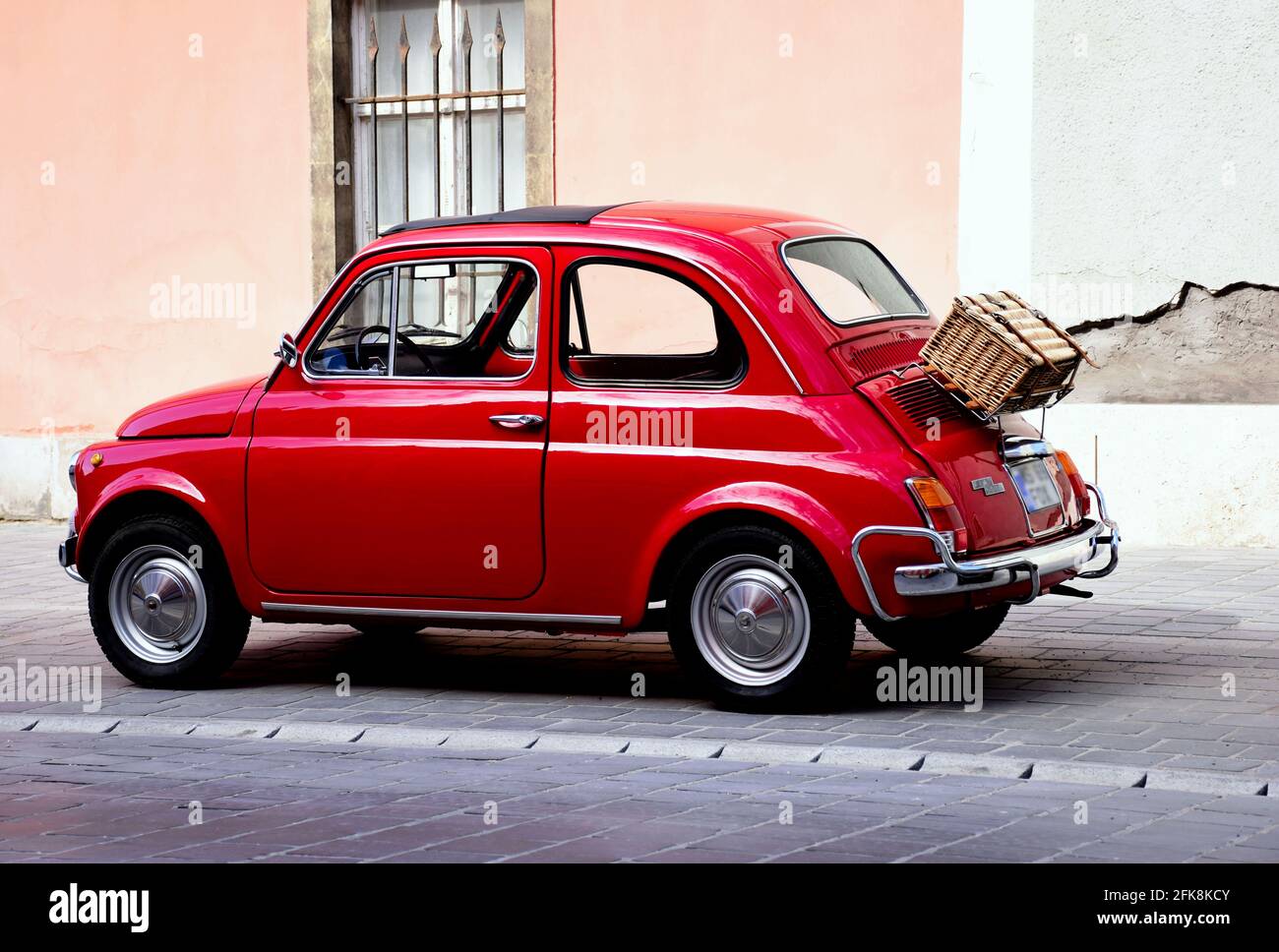 Petite voiture vintage italienne rouge élégante. Vue latérale. Ancienne façade en stuc de grunge à l'arrière-plan. Rangement en bois tissé et coffre à bagages sur le capot arrière Banque D'Images