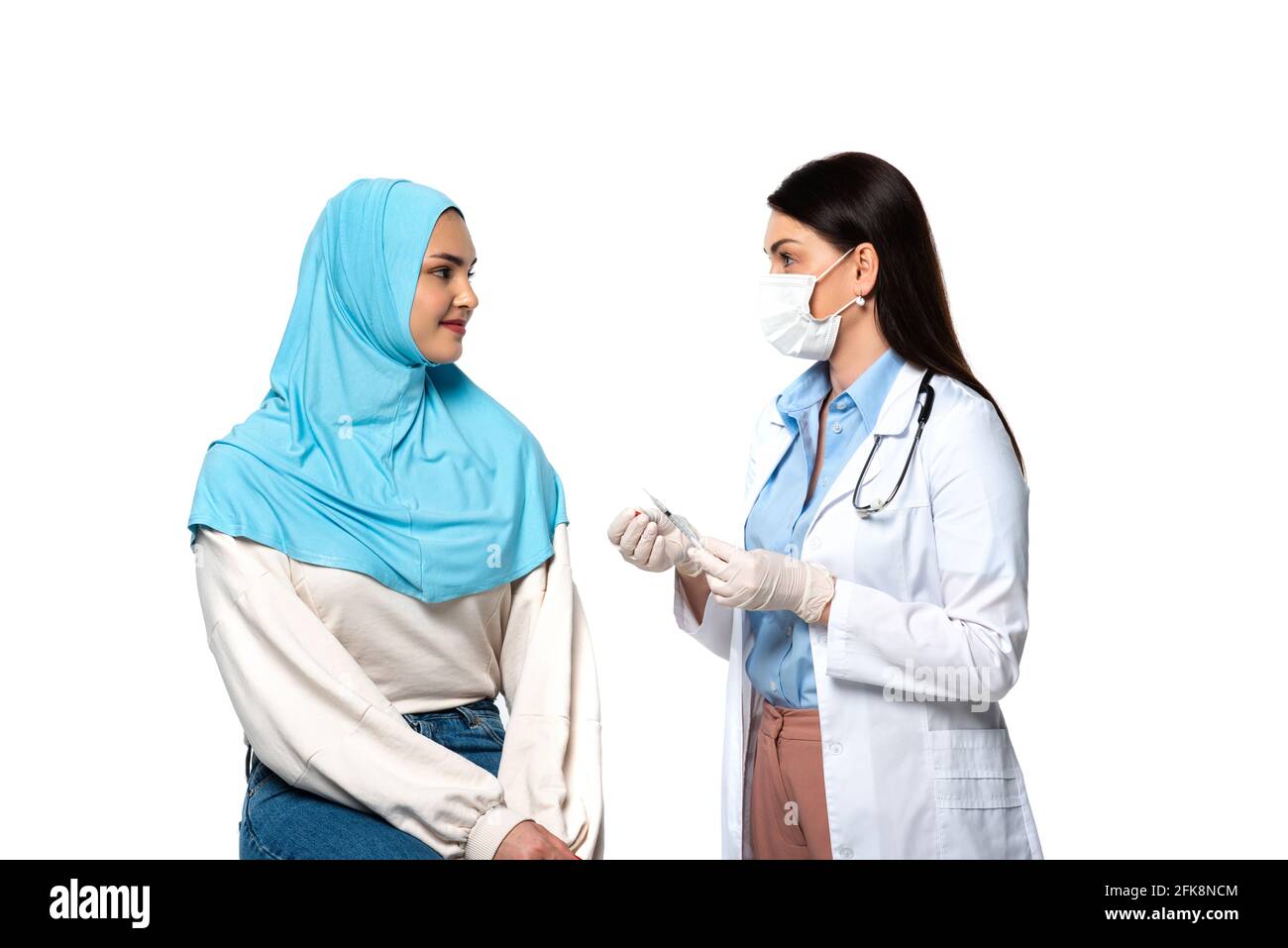 Médecin dans un masque médical tenant la seringue près d'un patient musulman isolé sur blanc Banque D'Images