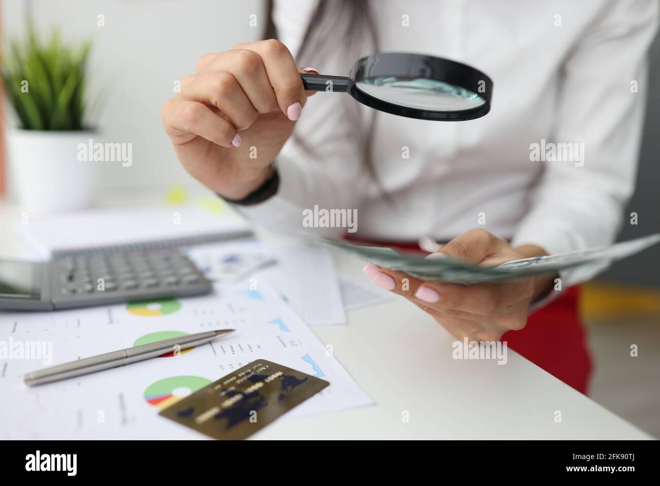La main féminine tient la loupe et l'argent à la table de travail Banque D'Images