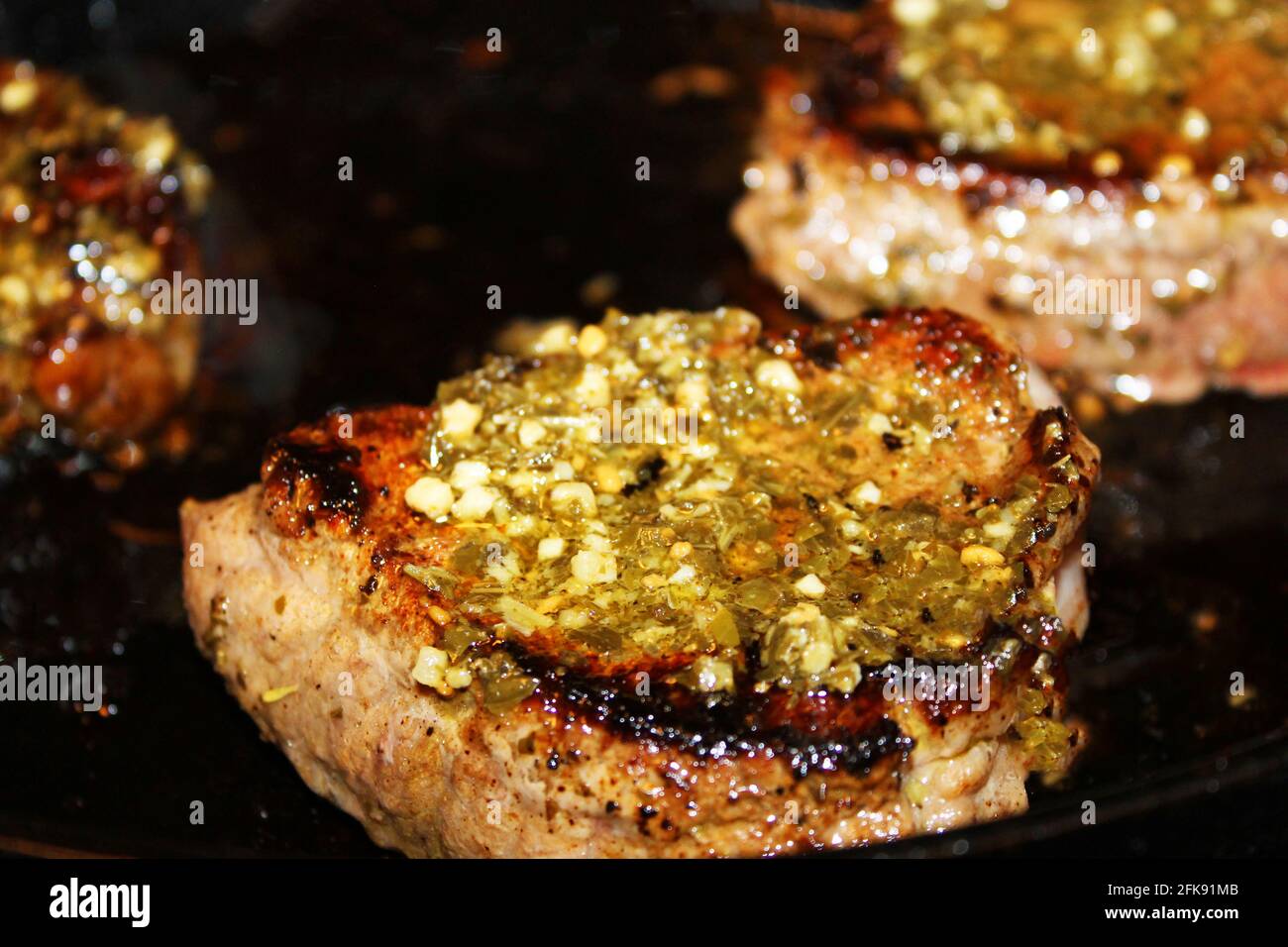 Gros plan de trois steaks avec sauce chimichurri cuisant dans une poêle à frire en fer. Banque D'Images