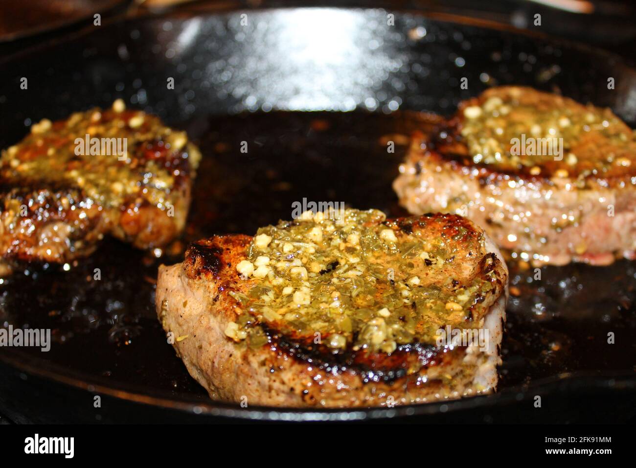 Gros plan de trois steaks avec sauce chimichurri cuisant dans une poêle à frire en fer. Banque D'Images