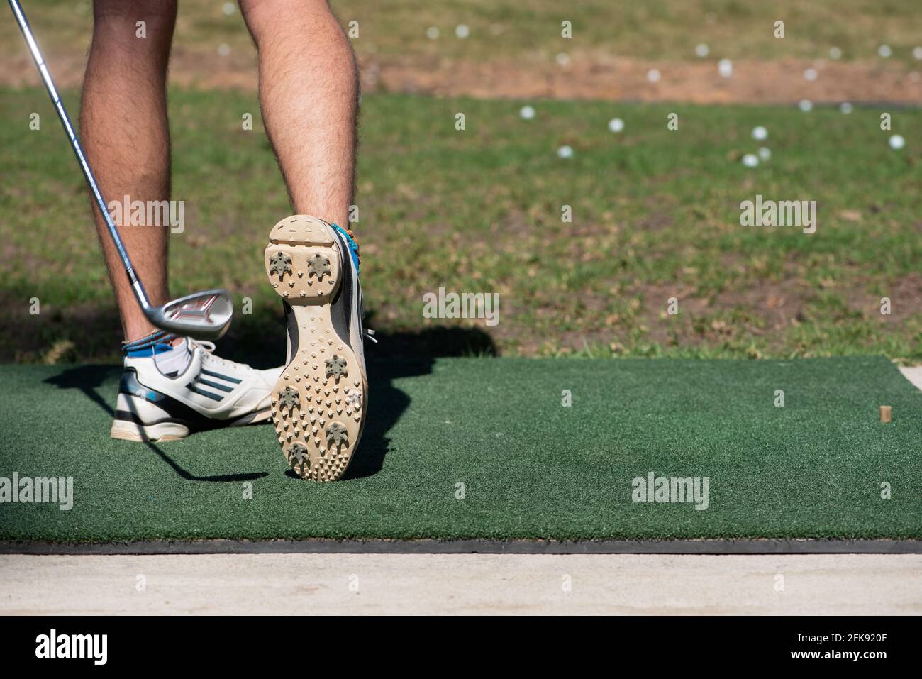 Gros plan d'un jeune homme qui frappe une balle de golf sur un terrain d'exercice avec le dessous de son golf chaussure visible Banque D'Images