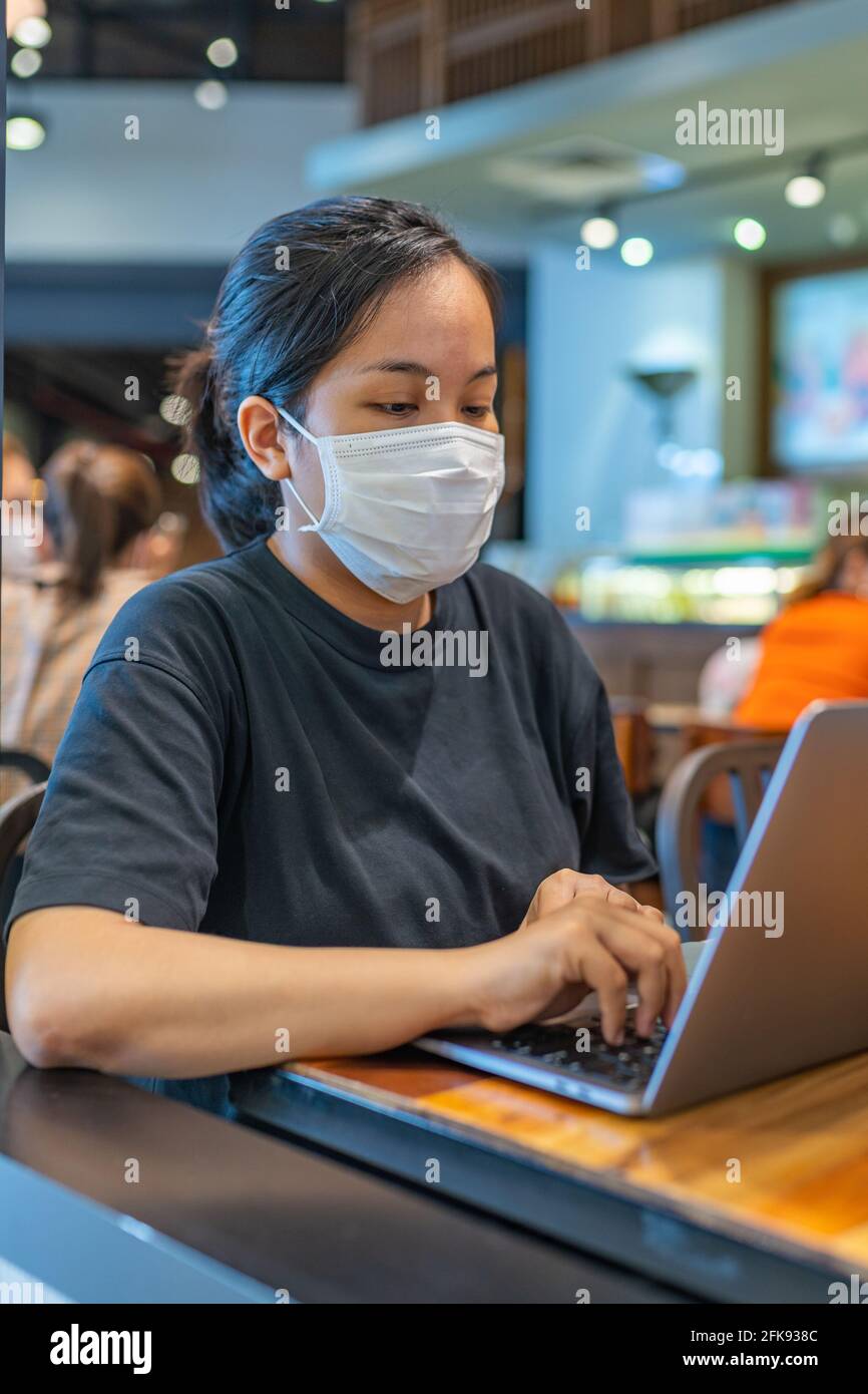 Portrait vertical d'une femme portant un masque de protection et utilisant un ordinateur portable Banque D'Images