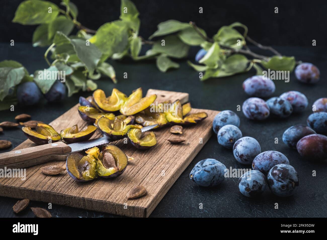 Prunes : prunes mûres en tranches et fruits entiers sur une planche en bois, fond sombre Banque D'Images