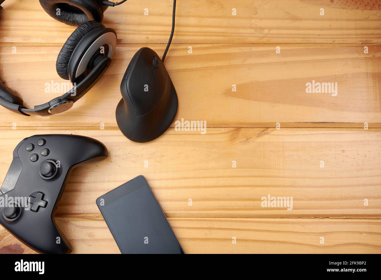 Vue de dessus des accessoires de jeu ergonomiques avec manette de jeu, souris verticale, casque et téléphone portable sur une table rustique en bois. Banque D'Images