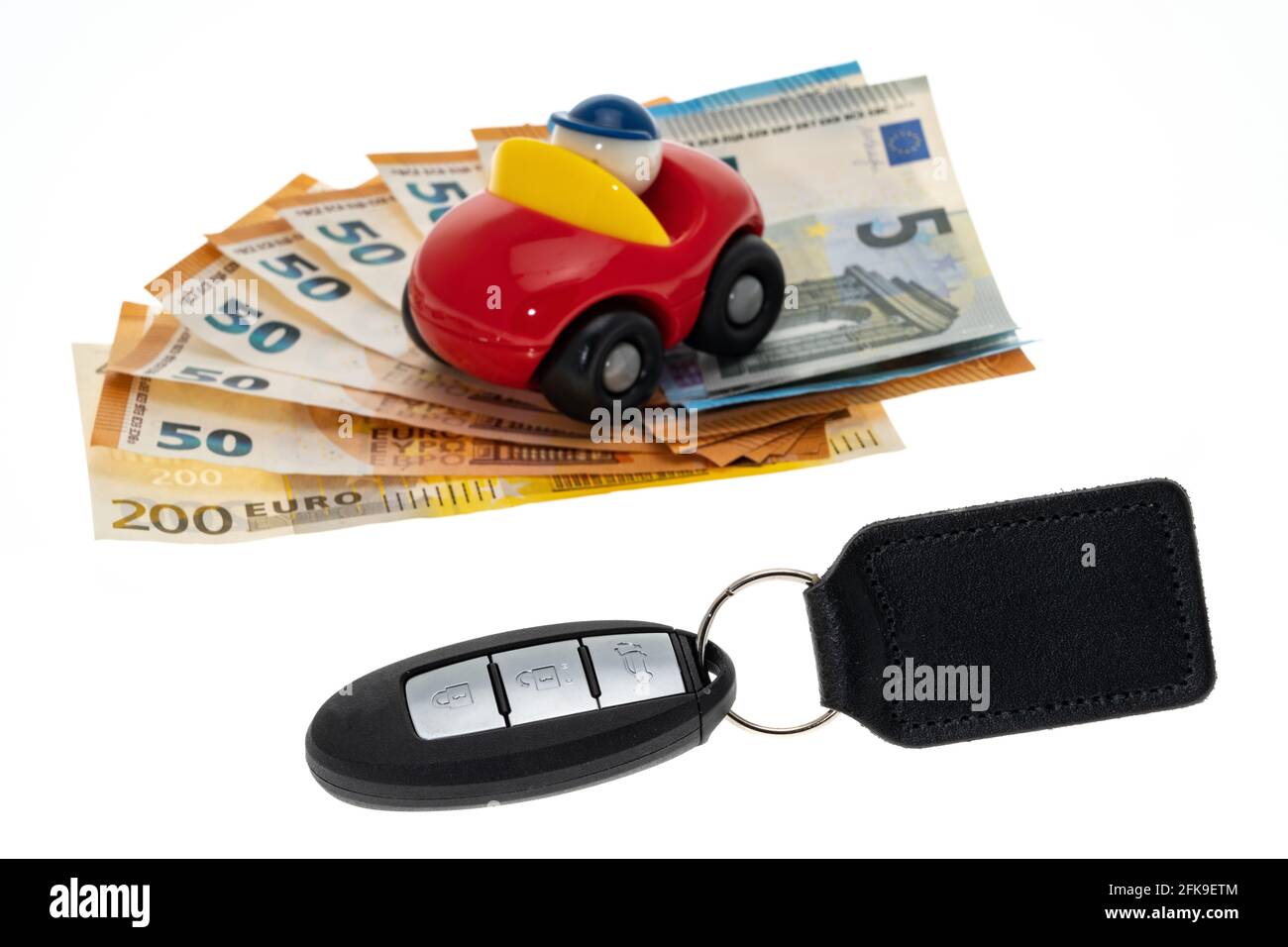 Une voiture-jouet placée au-dessus d'une pile de argent avec une clé de voiture - fond blanc Banque D'Images