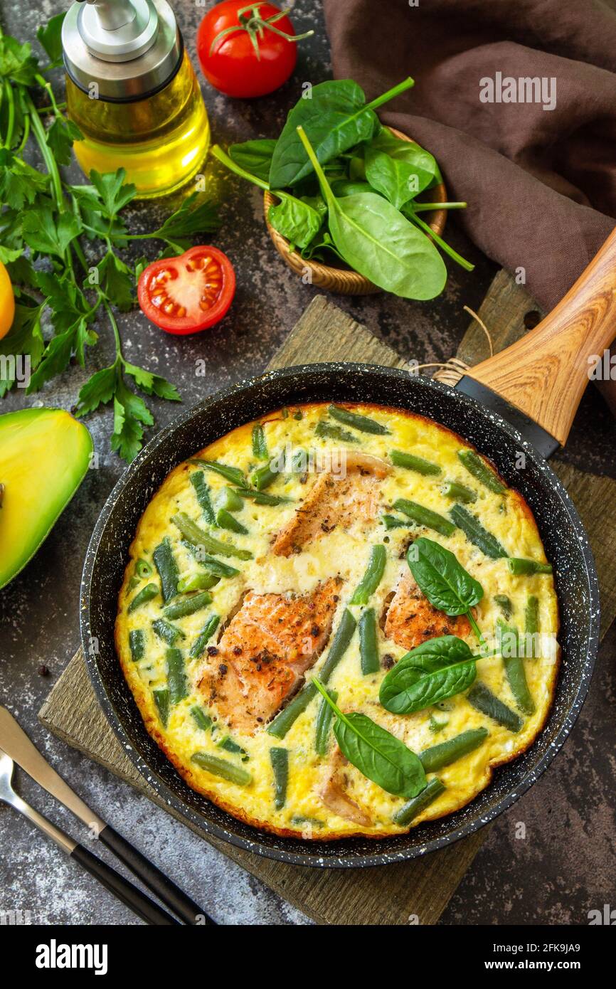 Petit déjeuner ou déjeuner en-cas. Omelette rustique (omelette, brouillée) avec filet de saumon et haricots verts dans une poêle sur fond de pierre. Banque D'Images