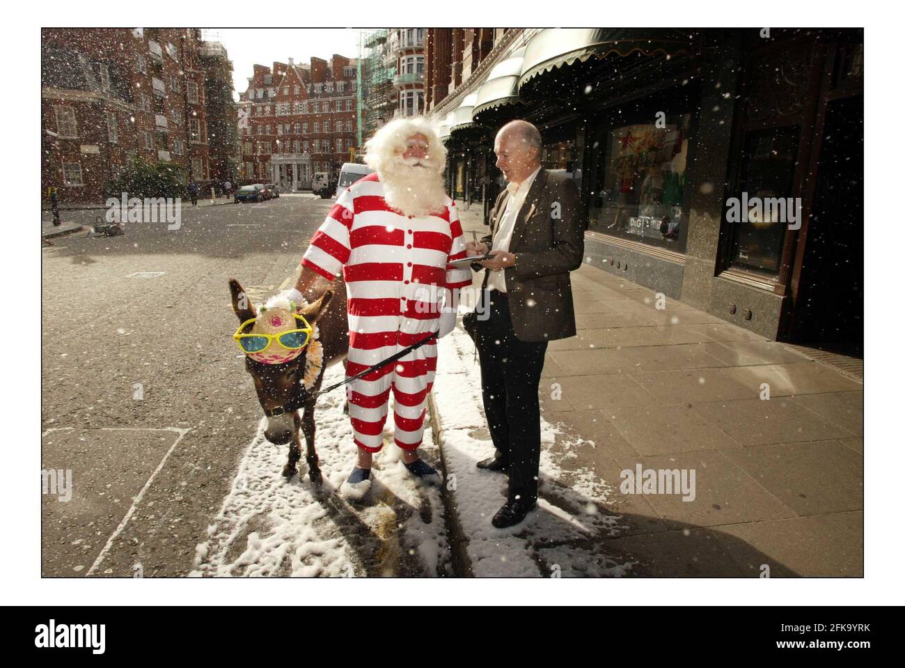 Le père Noël et son âne Dino en bord de mer posent pour des photographies devant un Harrods couvert de neige avant d'accueillir des invités dans la visite de Christmas World au troisième étage du magasin Knightsbridge, le 9 août 2005 à Londres, en Angleterre. Plus de 15 000 mètres carrés d'espace sont dédiés à Noël dans tout le magasin. Avec une machine à neige artificielle luttant contre la chaleur estivale, le Père Noël et son âne Dino arrivent devant une entrée enneigée de Harrods pour le lancement de Christmas World au magasin Knightsbridge à Londres. photo David Sandison 9/8/2005 Banque D'Images