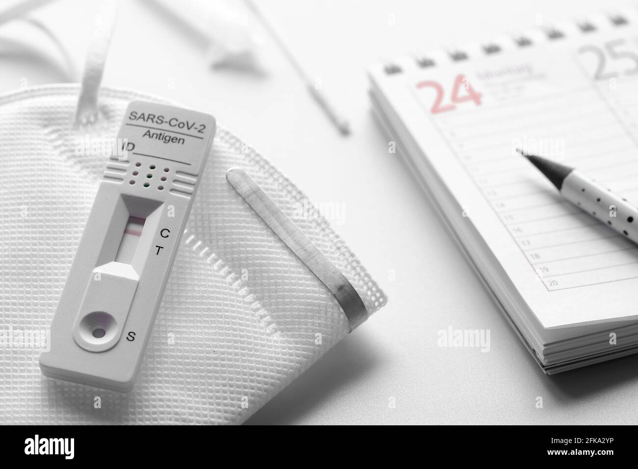 Planning hebdomadaire, schnelltest, test rapide de corona en langue allemande. Calendrier hebdomadaire et masque médical pp2 sur table blanche. Concept test-to-Go. Banque D'Images