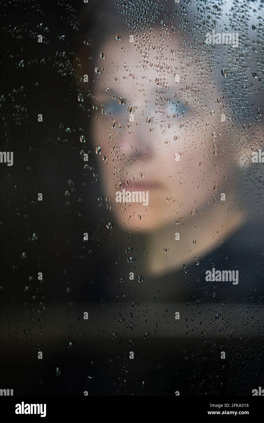 Femme dans des vêtements sombres regardant par la fenêtre dans le gouttes de pluie Banque D'Images