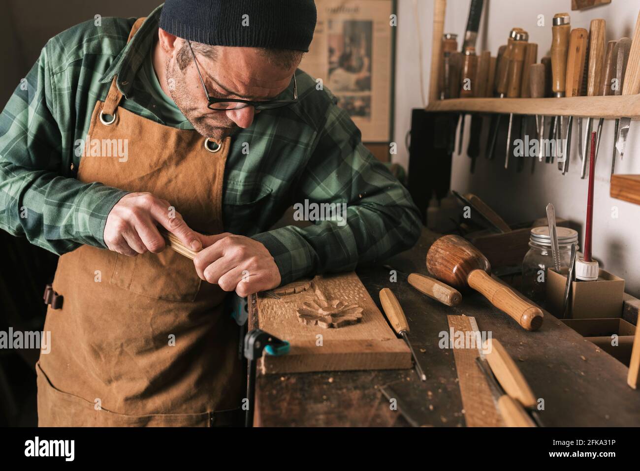 Vue latérale d'un ébéniste travaillant sur une sculpture en bois avec un burin. Banque D'Images