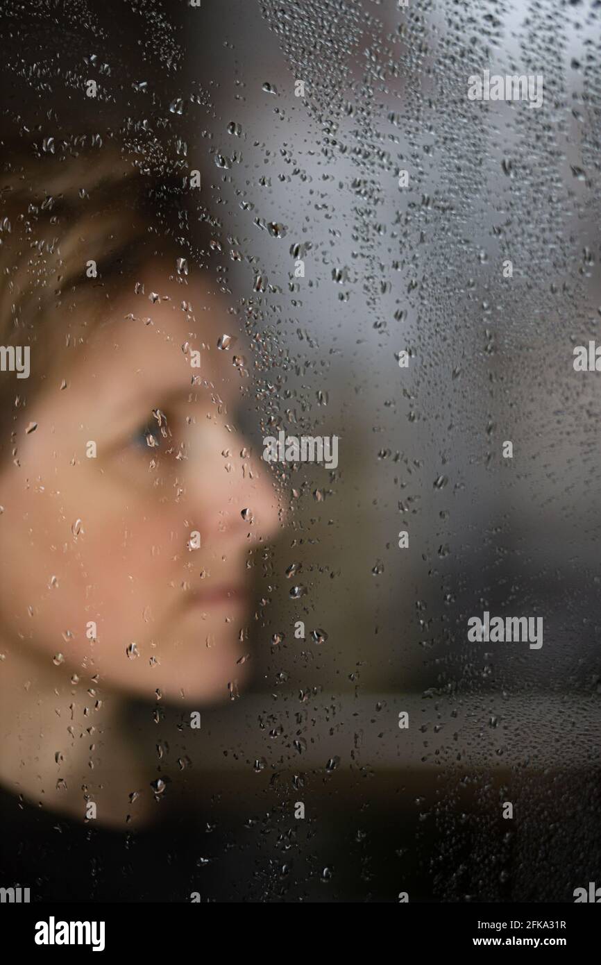 Le profil de la femme regarde la fenêtre dans les gouttes de pluie Banque D'Images