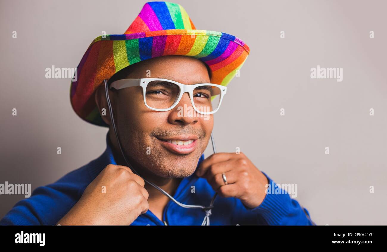jeune homme aux cheveux foncés avec chapeau de drapeau lgbt et lunettes blanches Banque D'Images