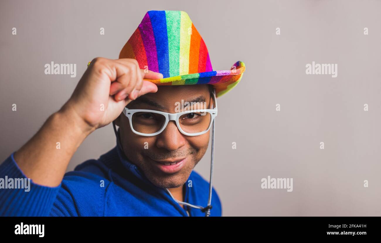 jeune homme aux cheveux foncés avec chapeau de drapeau lgbt et lunettes blanches Banque D'Images
