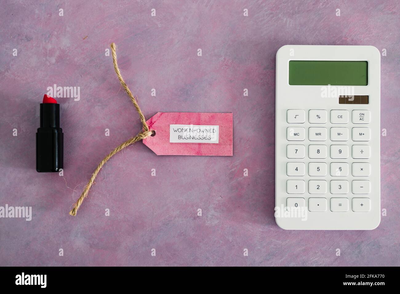 étiquette d'affaires pour femmes avec calculatrice et rouge à lèvres sur bureau rose, soutenant l'égalité et l'égalité des chances Banque D'Images