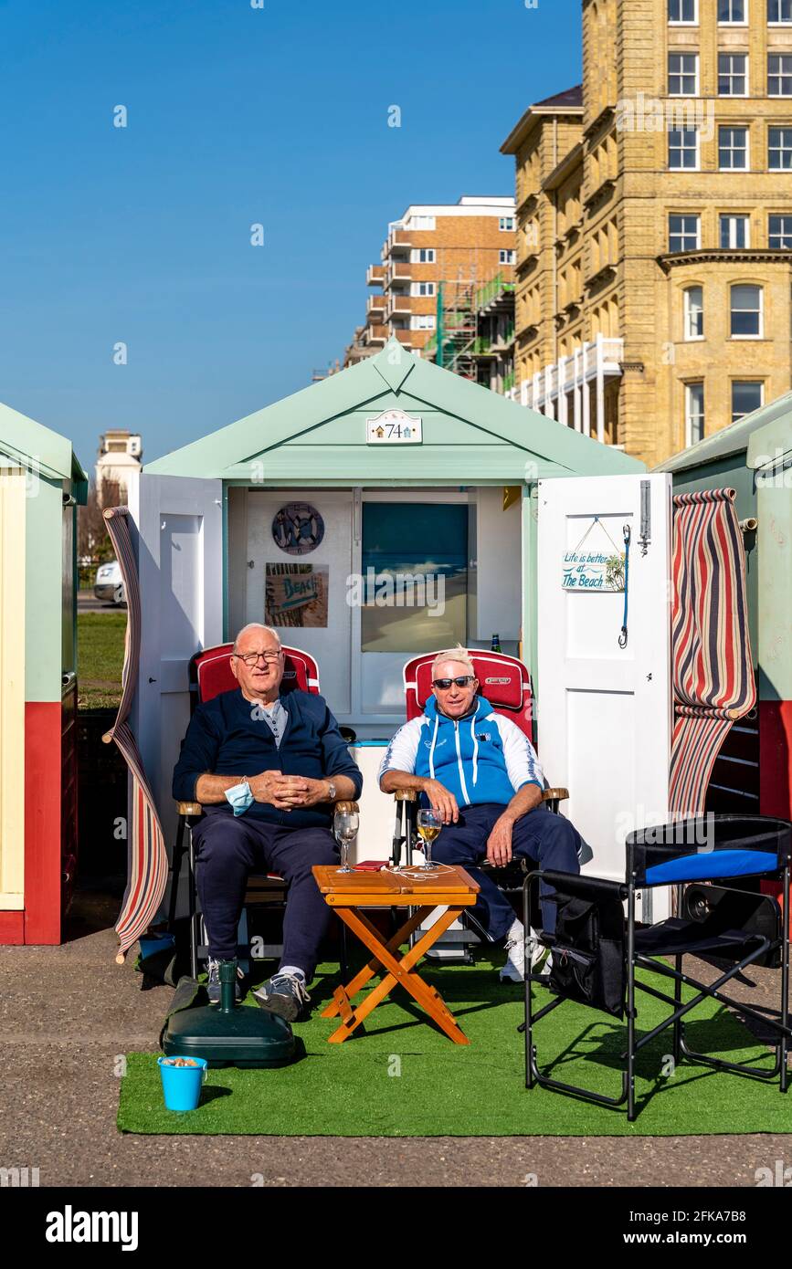 Deux hommes locaux appréciant le soleil à l'extérieur D'UNE cabane de plage sur le front de mer de Hove, Brighton, East Sussex, Royaume-Uni. Banque D'Images